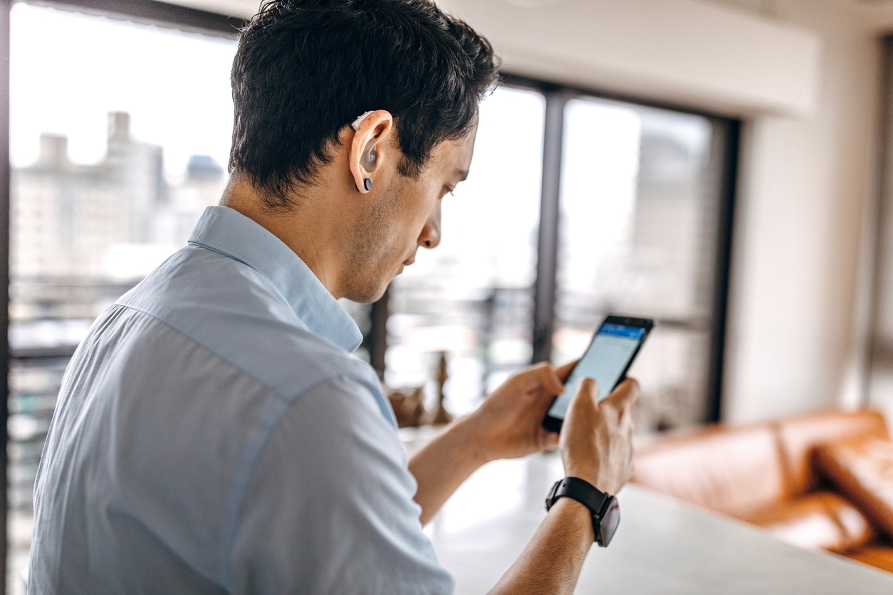 Man wearing a hearing aid checking his phone.