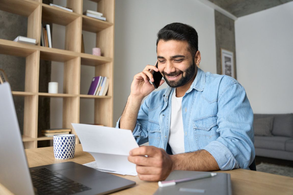 man smiling on the phone while looking at paper